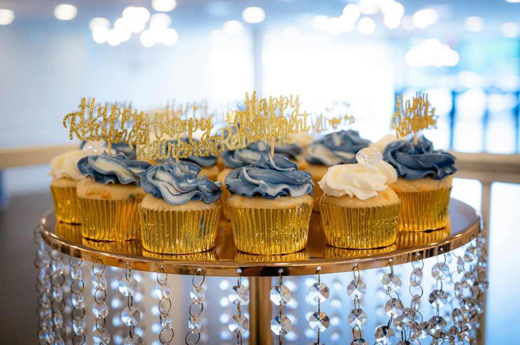 Blue and yellow cupcakes with toppers that say happy retirement in gold glitter.