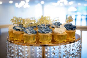 Blue and yellow cupcakes with toppers that say happy retirement in gold glitter.