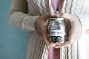 Person holding a clear glass jar with a "savings" label on it and money inside.